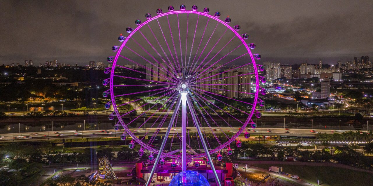 Agora é oficial! Escape Hotel inagura jogo de escape missão secreta na roda rico (1) Roda Rico brilhando em luz roxa durante a noite com cidade e parque no fundo
